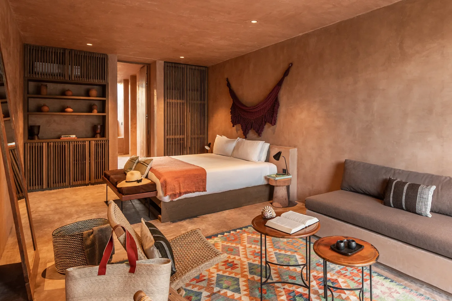 King bed with a crimson hammock wall hanging, sofa and lounge chairs