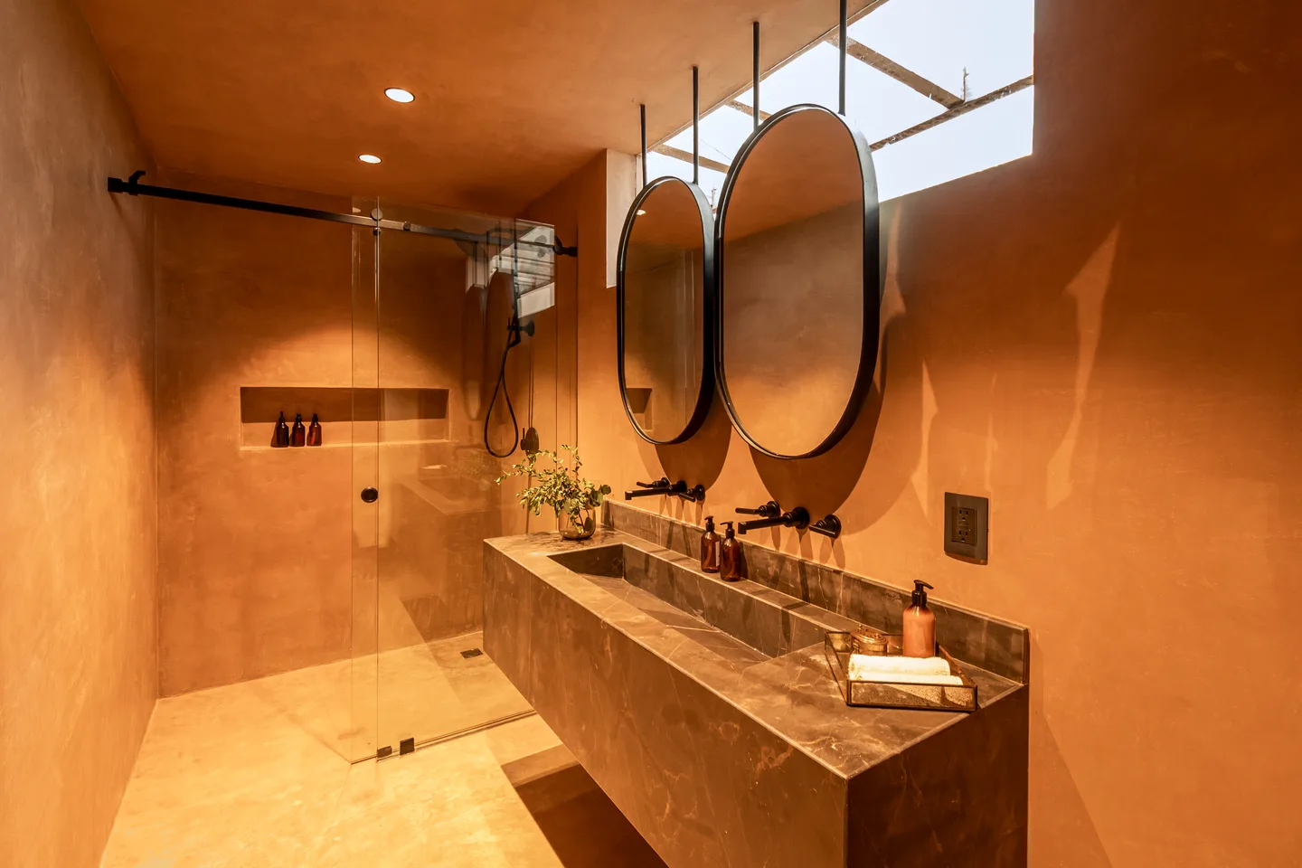 Baño con ducha de cristal a ras de suelo, lavabo de piedra y dos espejos ovalados