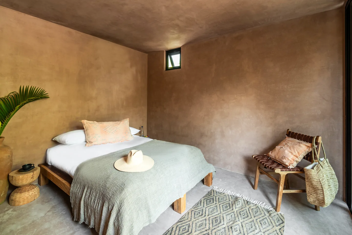Queen bed with a sage throw, leather lounge chair and potted palm