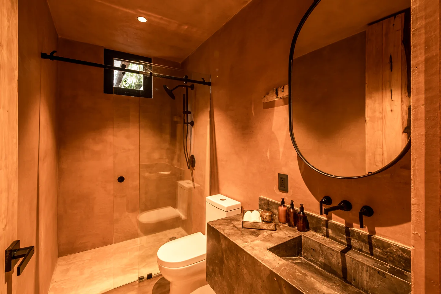 Baño con regadera de vidrio, lavabo de piedra y espejo ovalado