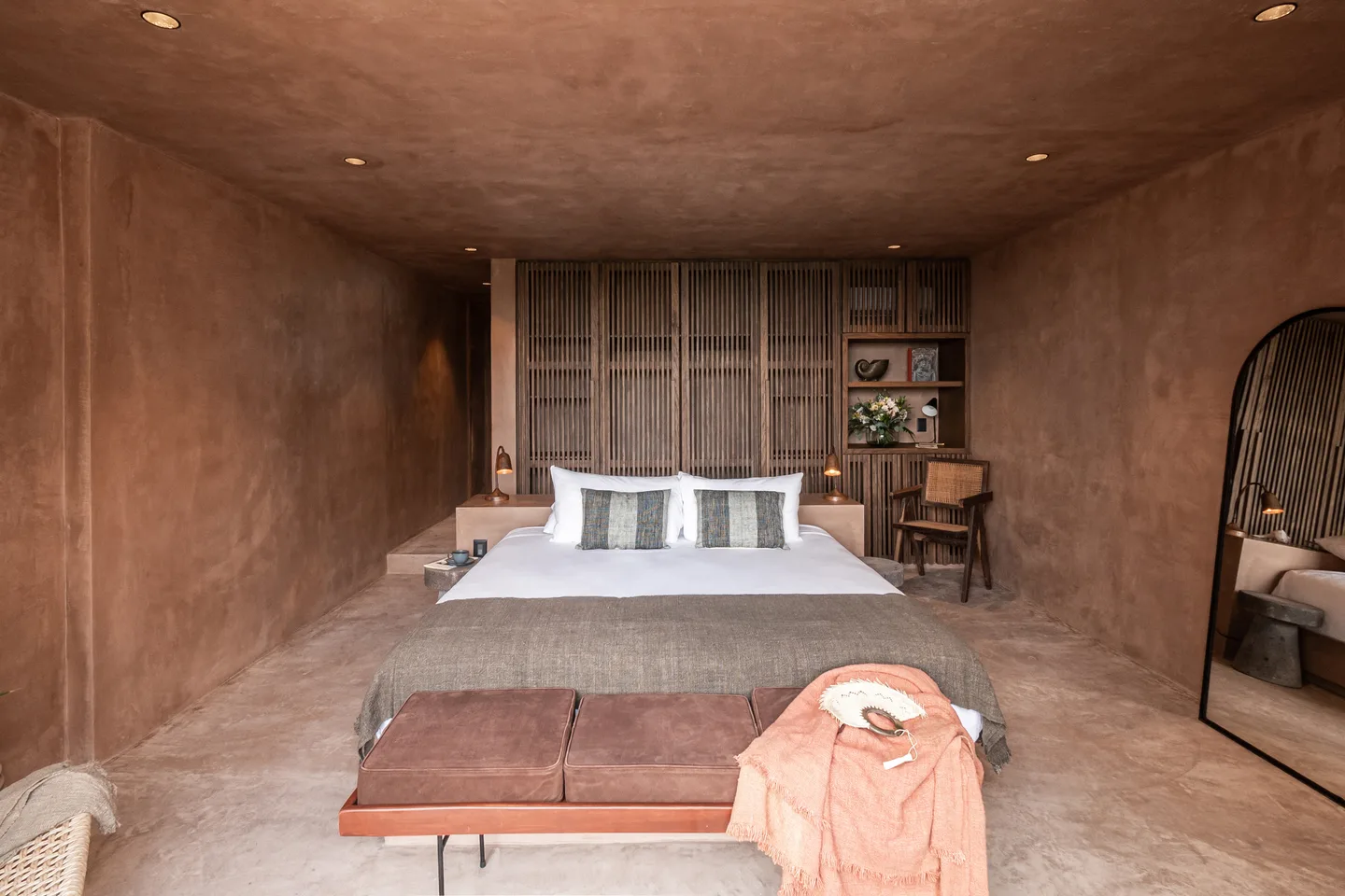 King bed with leather bench in front of a latticed wooden wall