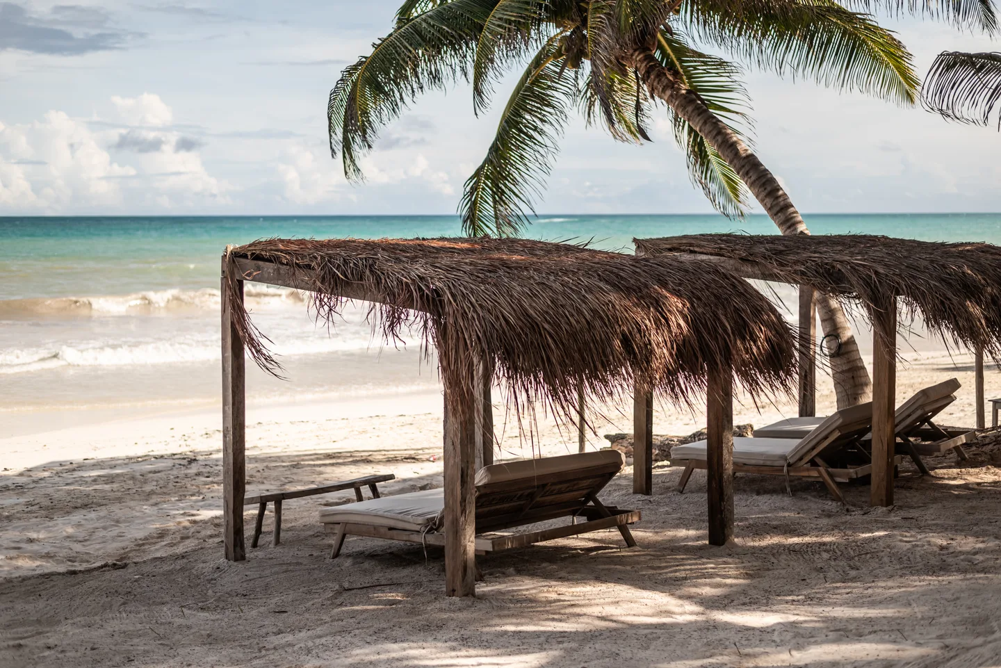 Row of thatched palapas with sun loungers on the white sand beach