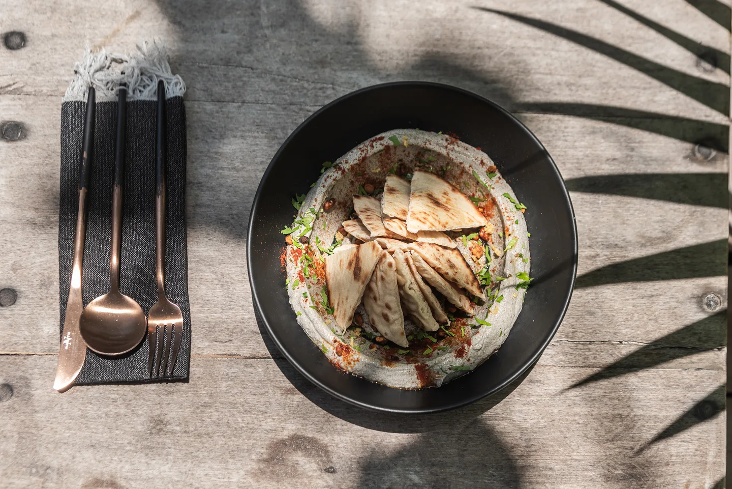 Dip topped with flatbread triangles in a black bowl on a weathered wood table