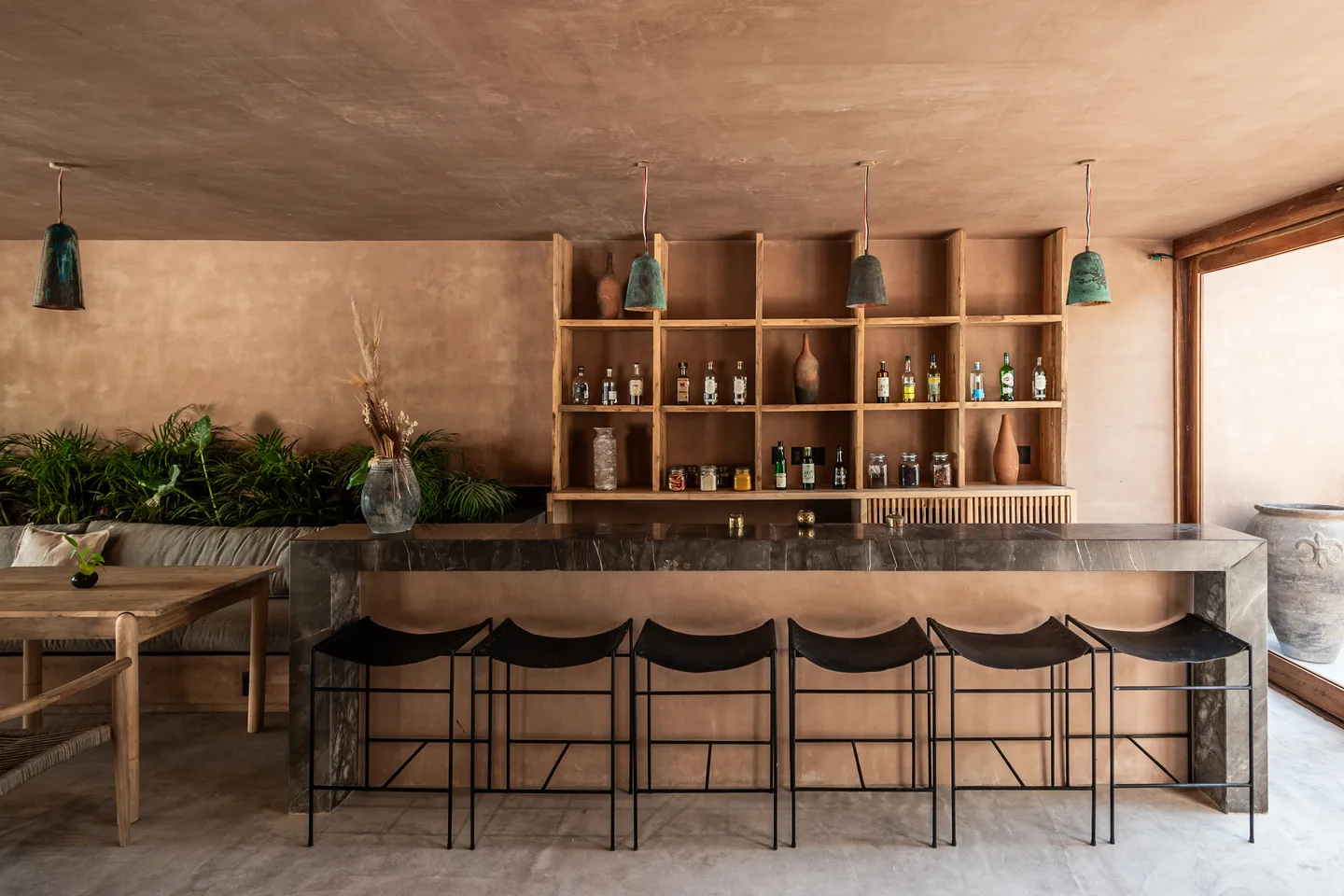 Stone bar with black stools in front of open shelving of bottles and ceramics