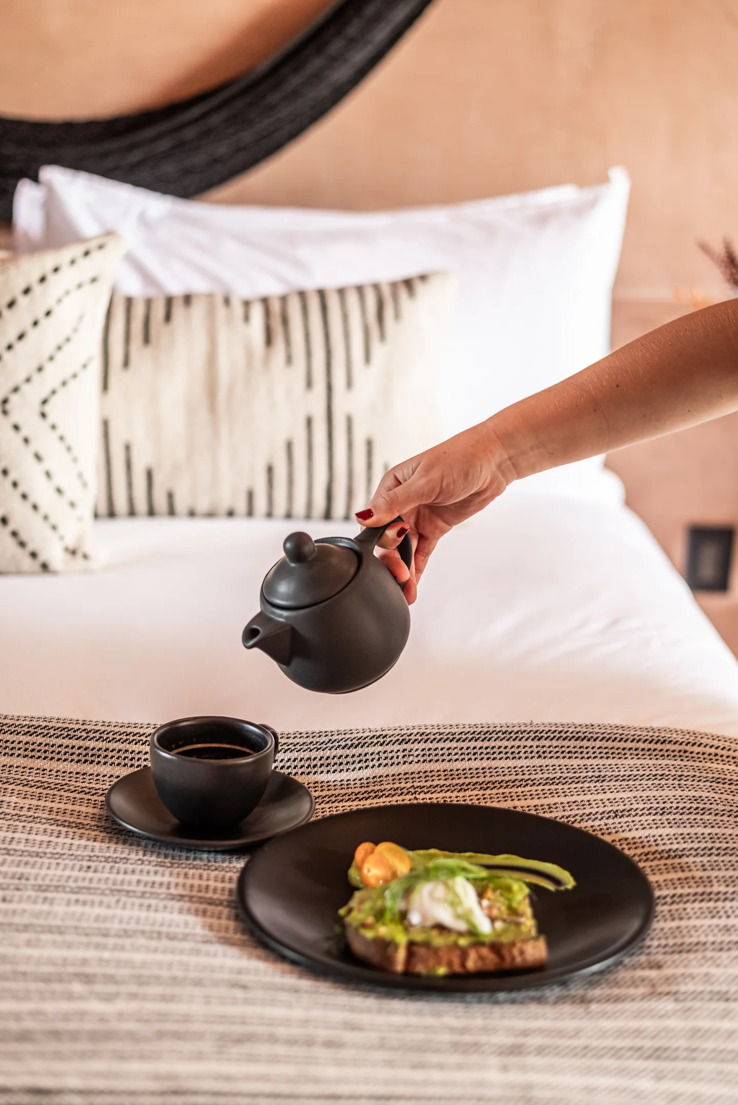 Tea being poured beside avocado toast served on the bed