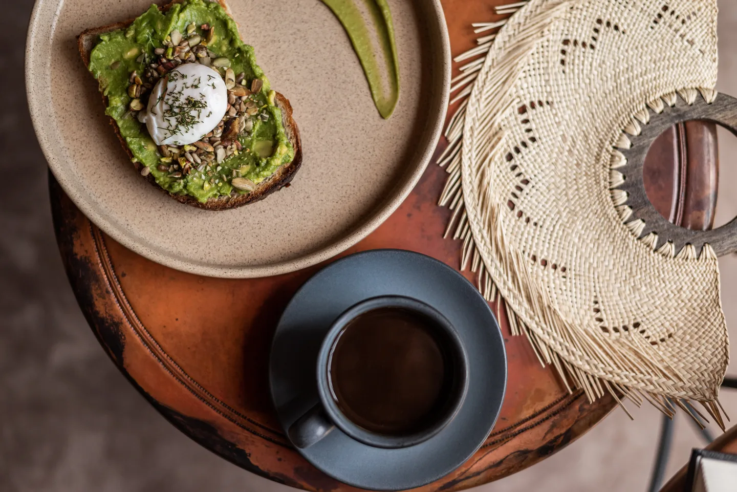 Avocado toast with a poached egg and black coffee on a terracotta tray, seen from above