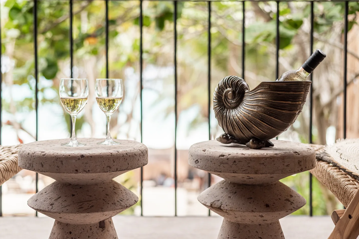 Two glasses of white wine and a bottle chilling in a shell-shaped cooler on a suite balcony