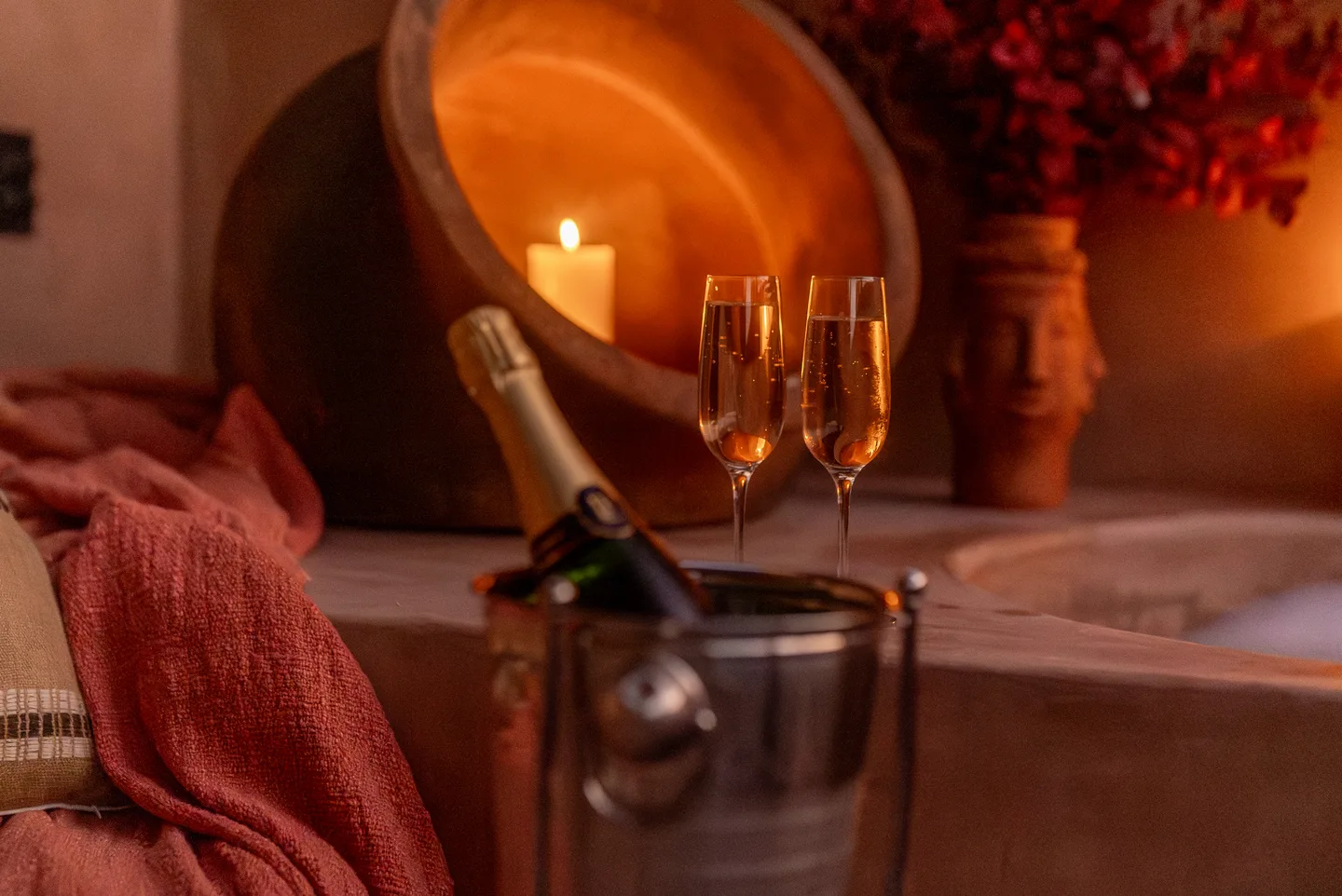 Champagne on ice with two glasses beside a candlelit soaking tub