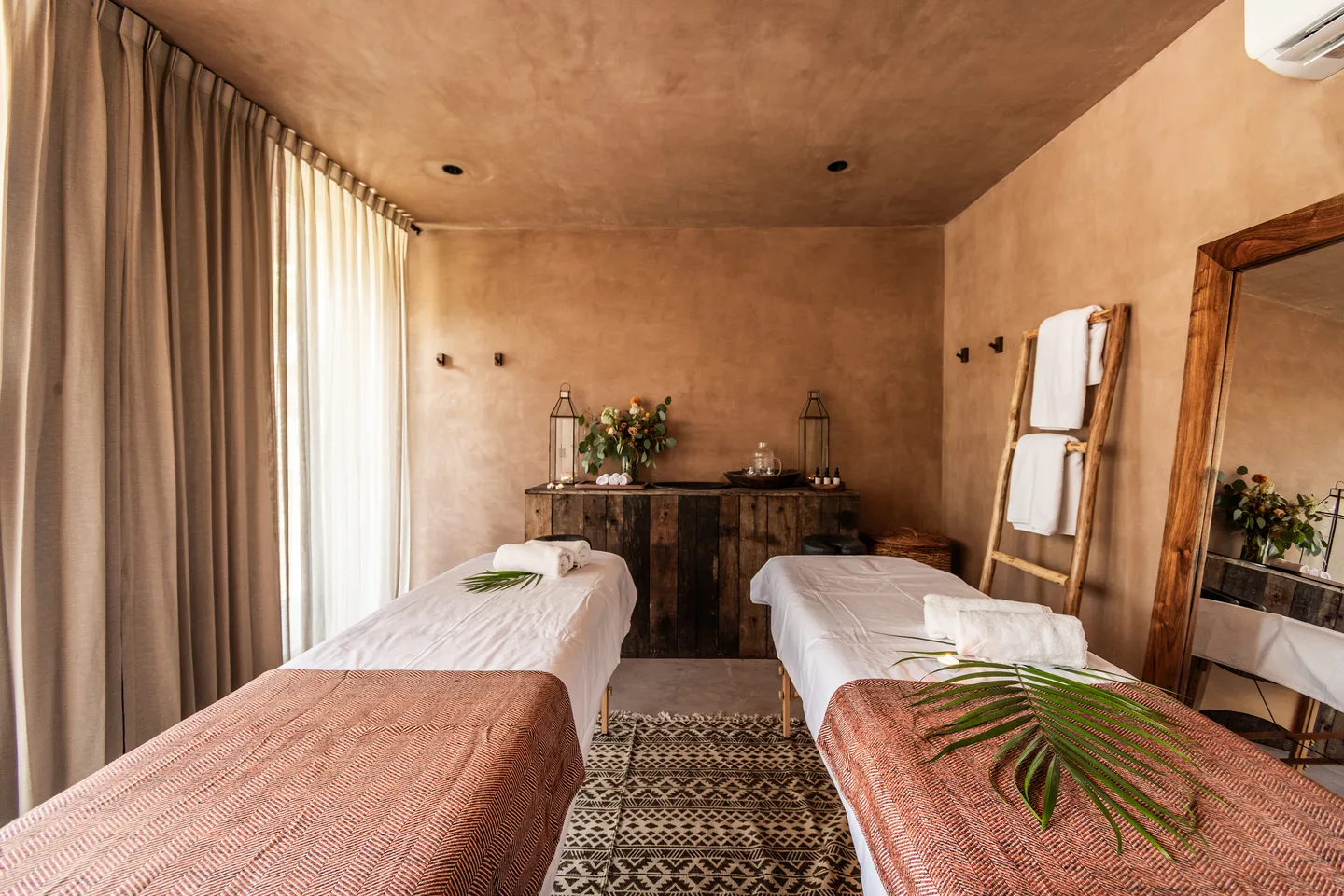 Spa treatment room with two massage beds dressed in woven throws and a palm leaf