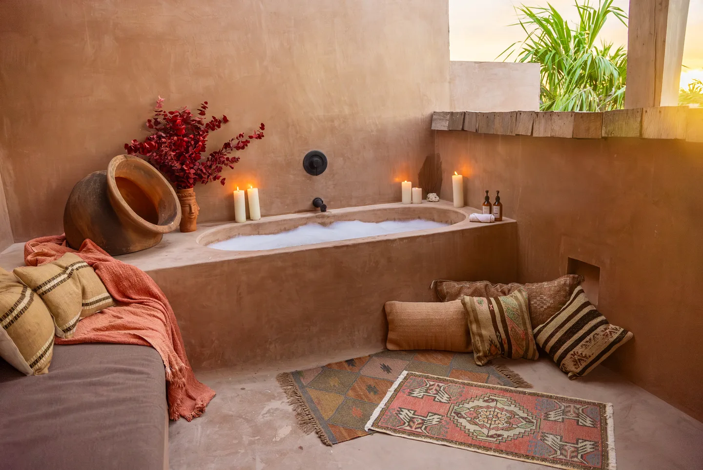 Outdoor soaking tub filled with foam, surrounded by candles, cushions and kilim rugs
