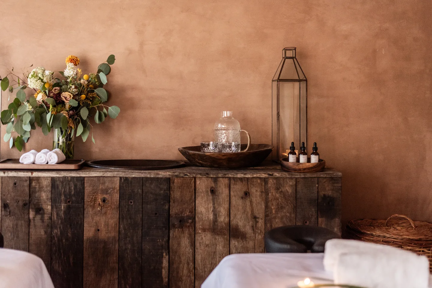 Spa console of reclaimed wood with flowers, a lantern, oils and rolled towels