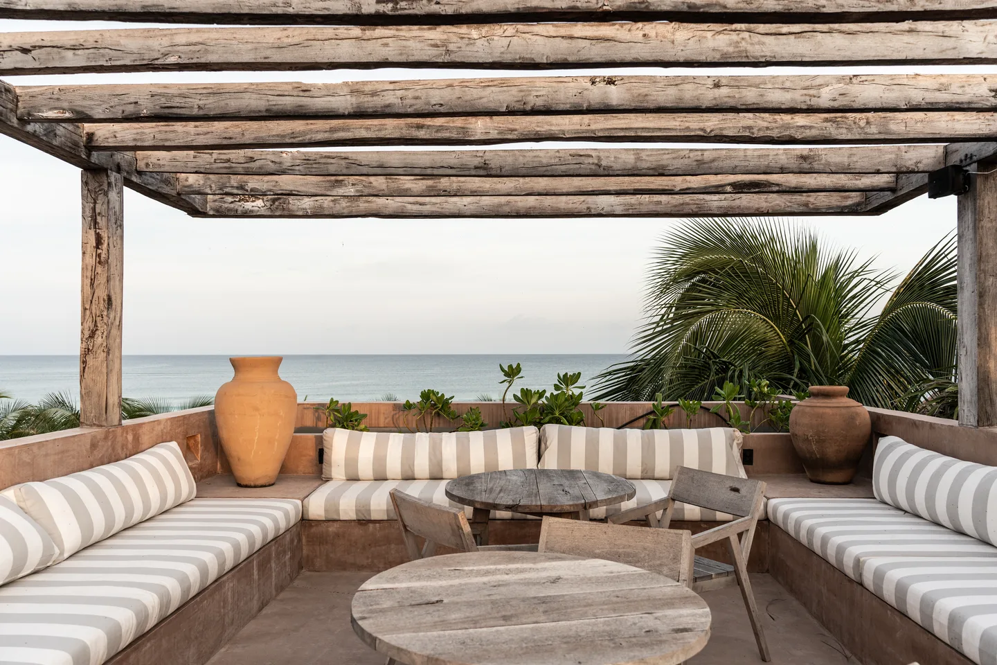 Rooftop pergola lounge with striped cushions and a round wooden table facing the sea
