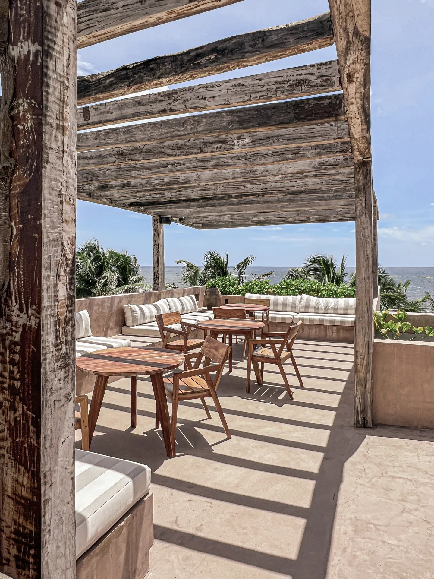 Rooftop dining tables in the shade of a driftwood pergola with sea views