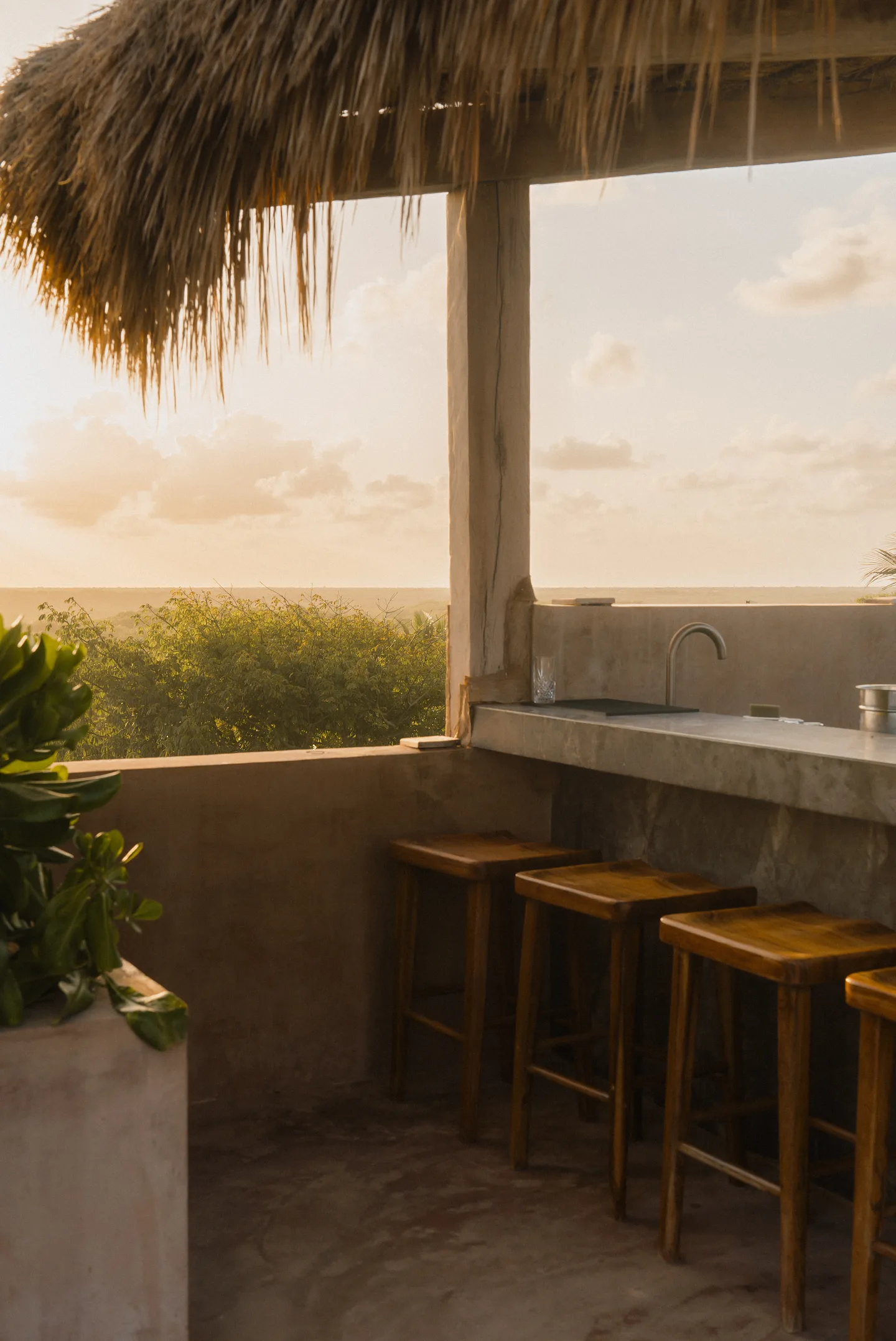 Rooftop bar with wooden stools under a thatched roof at sunset