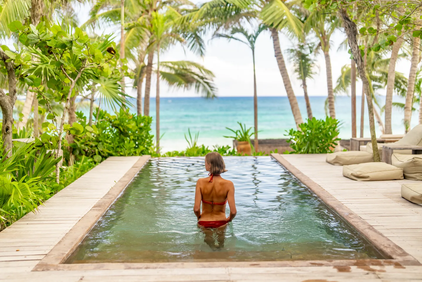 Guest standing in the pool looking toward the sea through the palms