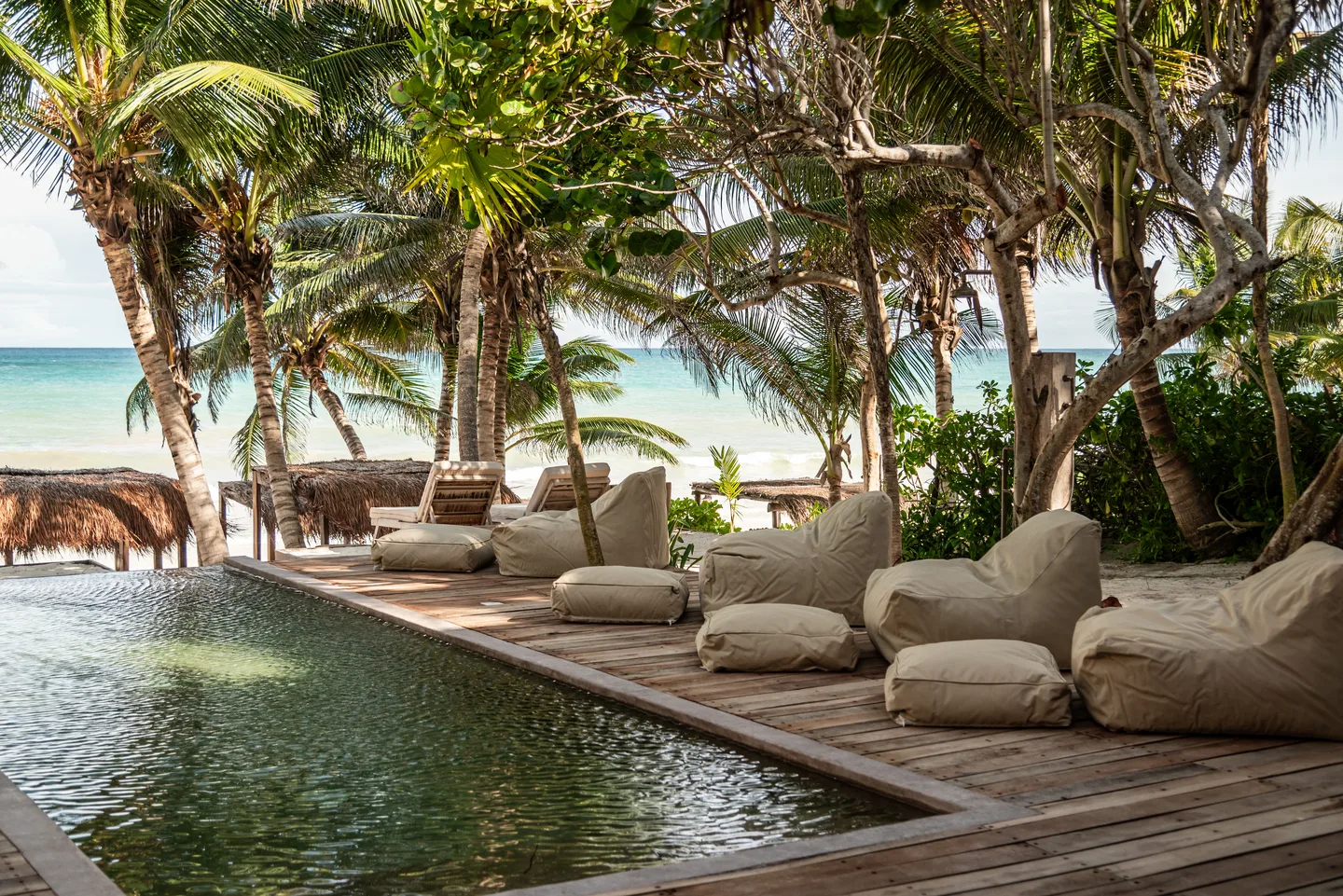 Oversized canvas loungers on the wooden pool deck with the beach beyond