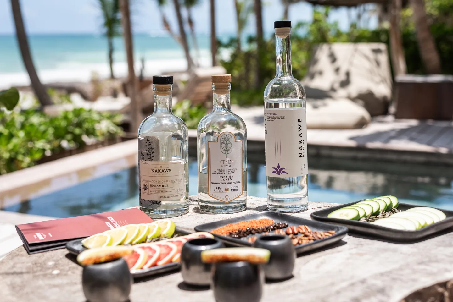 Three bottles of Nakawé mezcal with citrus, chocolate and tasting cups beside the pool