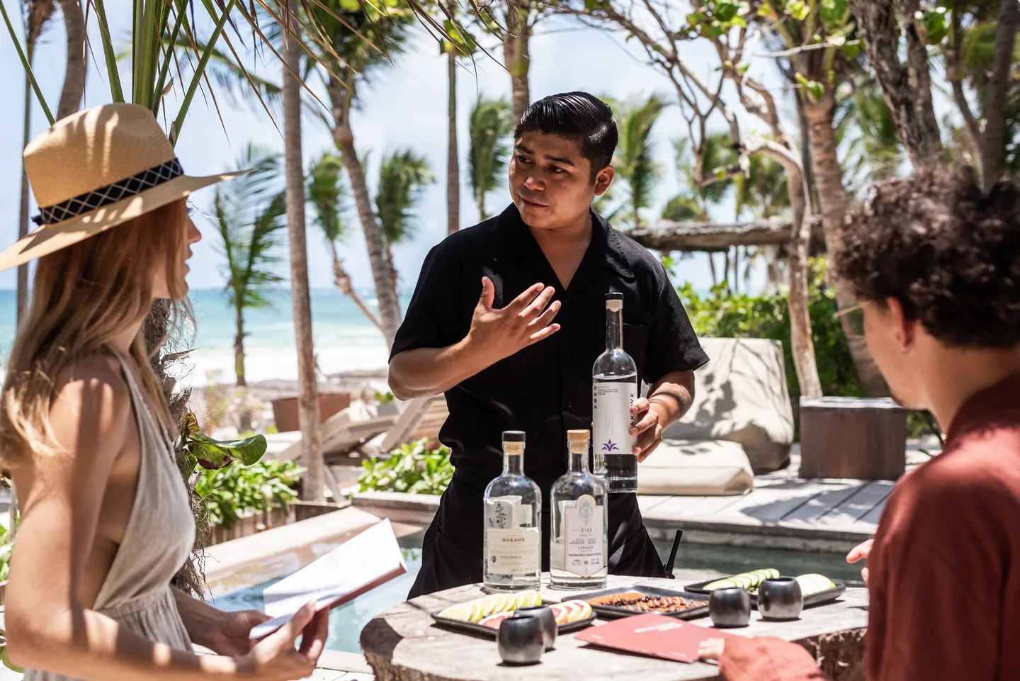Host presenting a mezcal tasting to two guests by the pool