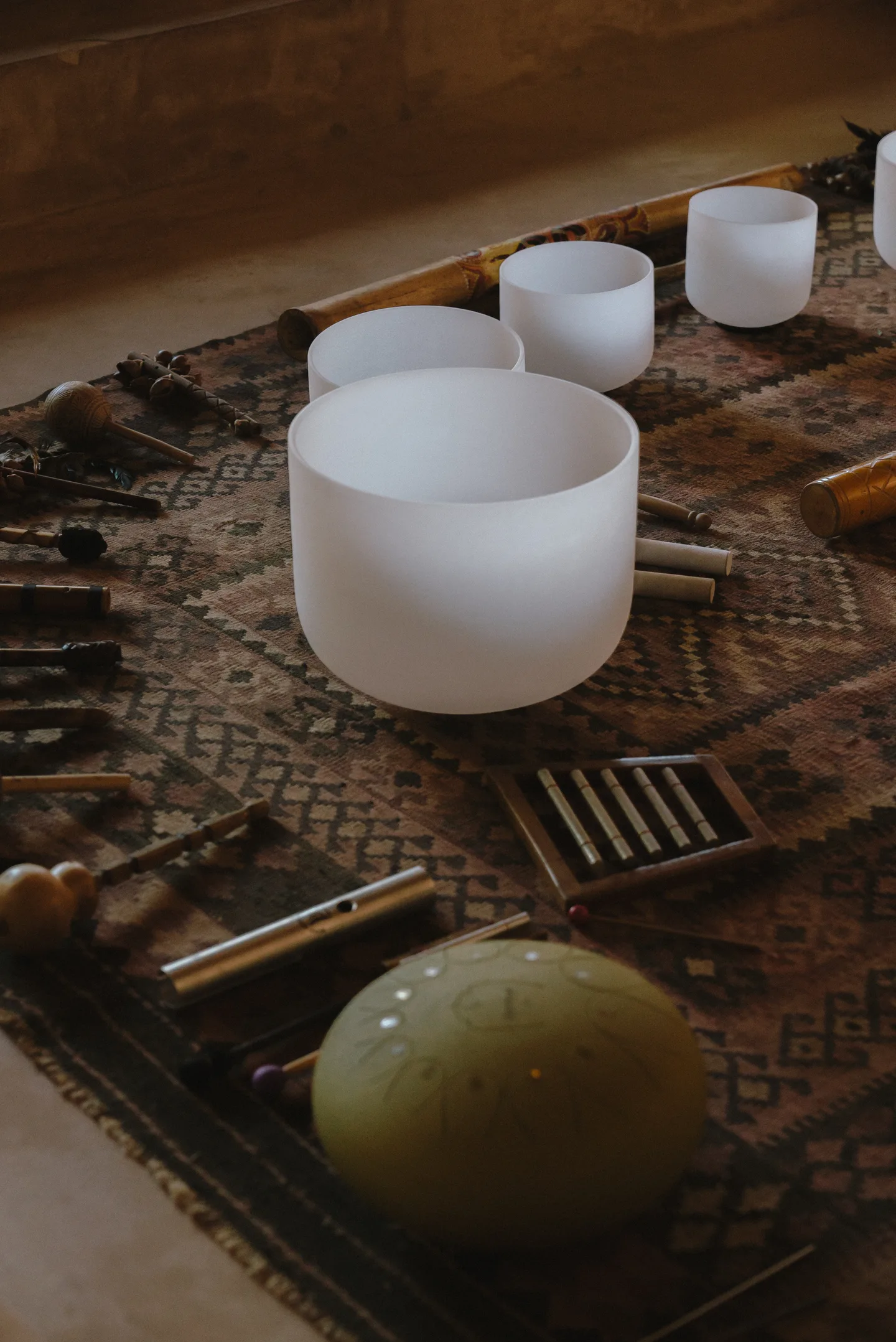 Crystal singing bowls, a tongue drum and chimes laid out on a woven rug