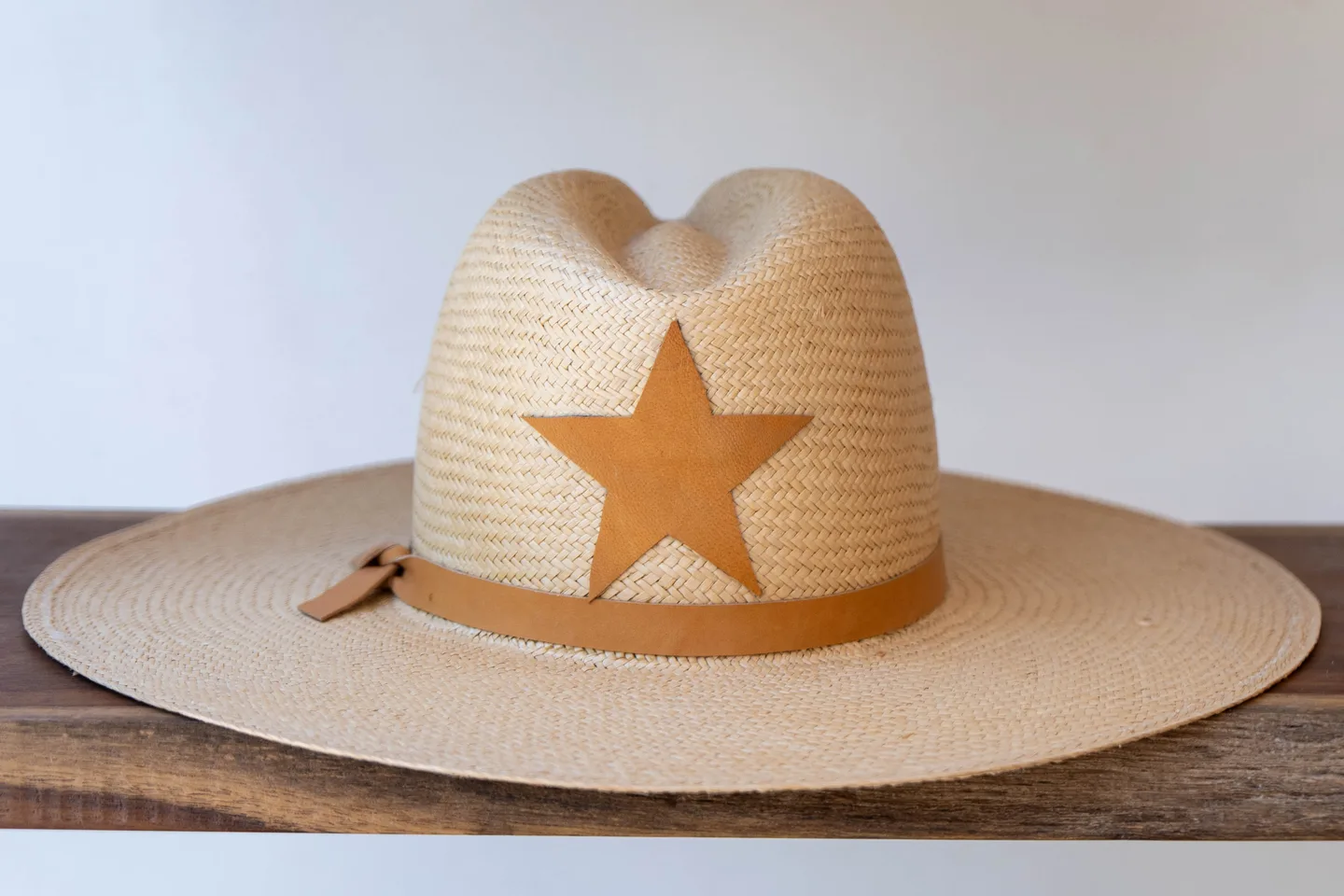 Woven straw hat with a leather star on a wooden shelf