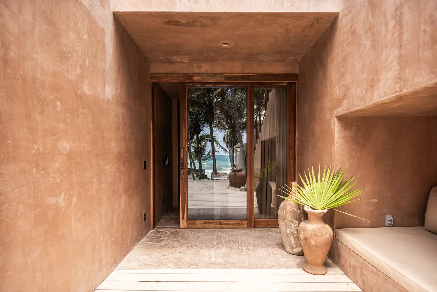 Vestíbulo de entrada de la suite Caracol con banco integrado y puertas de vidrio que se abren hacia la playa