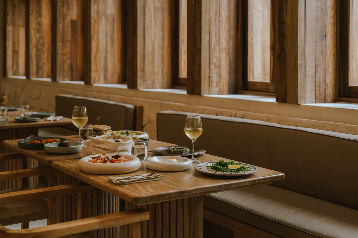 Climo dining room with wooden tables set for lunch along a banquette beneath shuttered windows