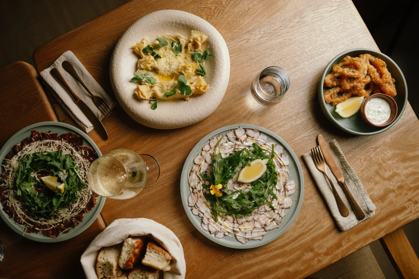 Table at Climo with ravioli, carpaccio, fried calamari, bread and white wine, seen from above