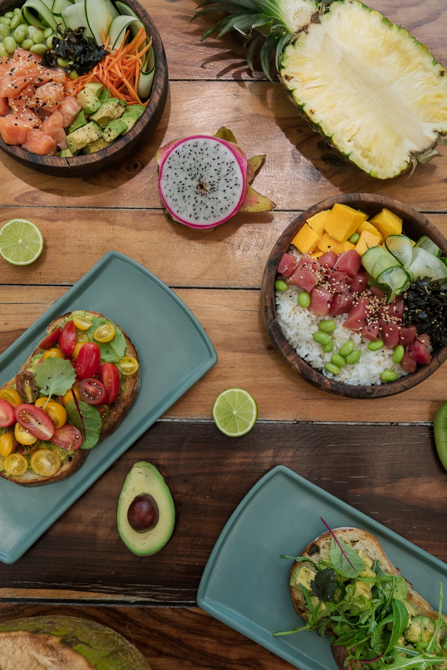 Poke bowls, salads and fresh tropical fruit on a wooden table, seen from above
