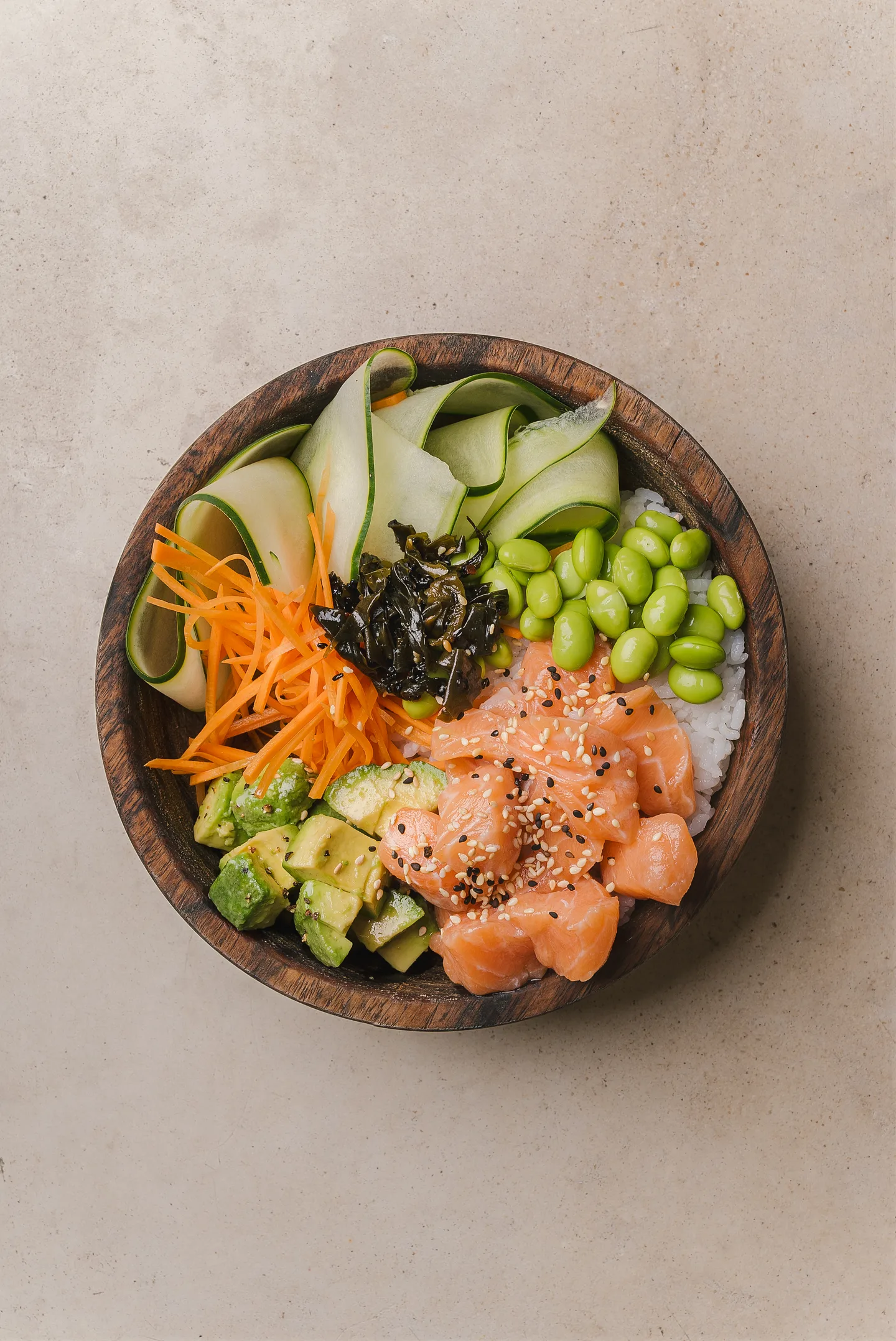 Salmon poke bowl with edamame, avocado, carrot and cucumber in a wooden bowl