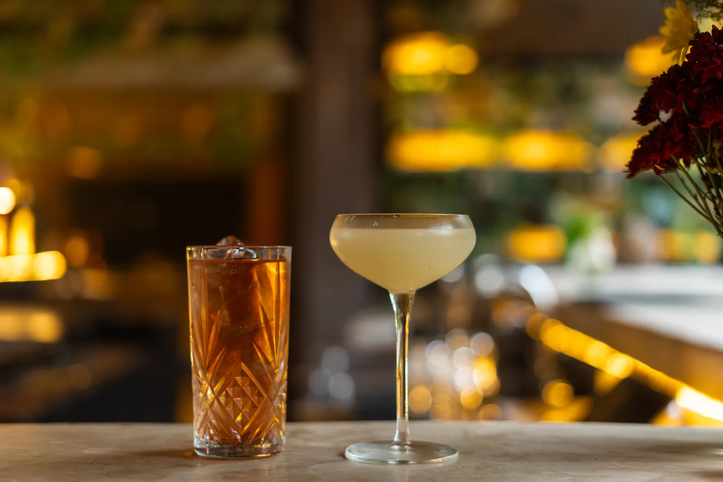 Two cocktails on the bar at NÜ Tulum with warm lights behind