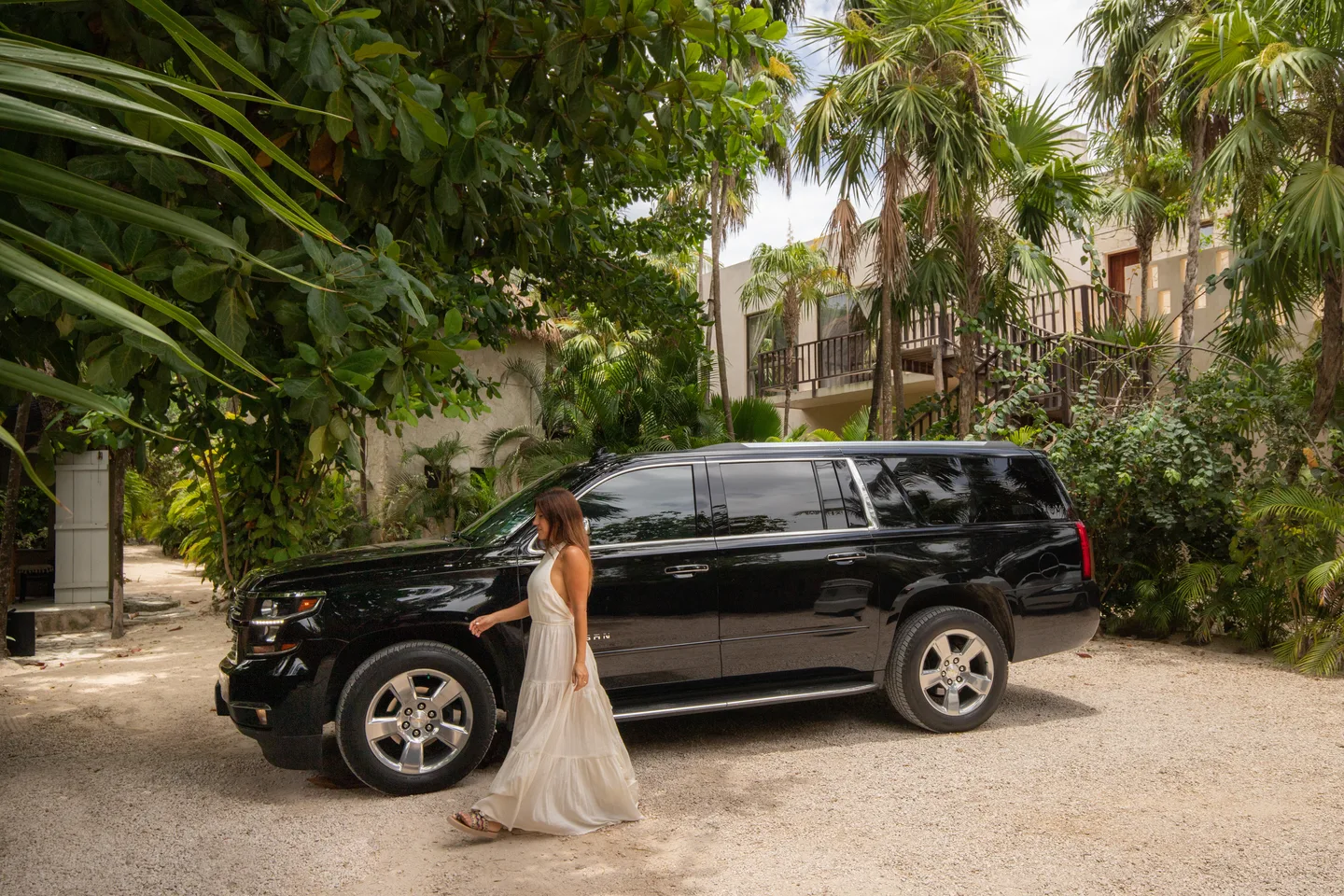 Guest walking to a black private SUV on a palm-lined Tulum lane
